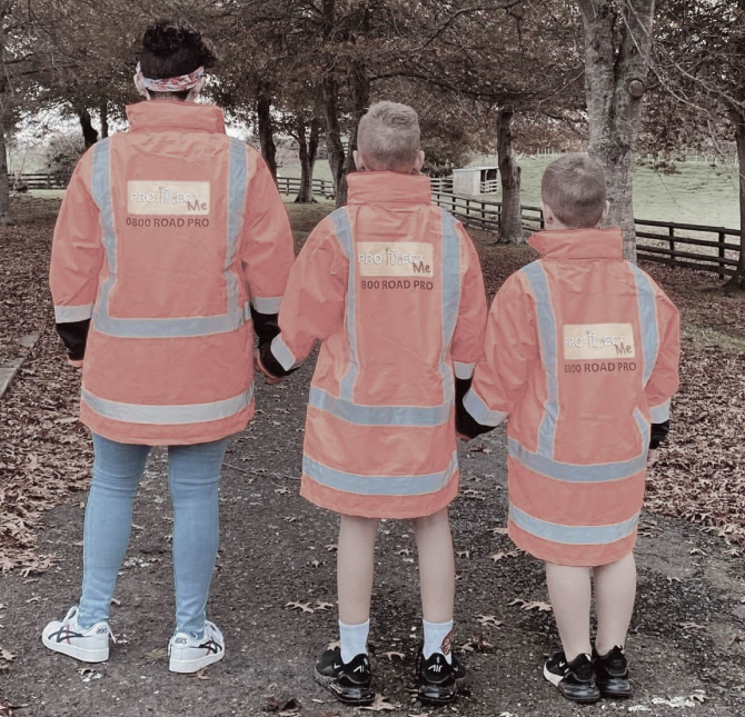 Adult and two children wearing Pro-Tect Me high-vis orange jackets in a park on the walk path
