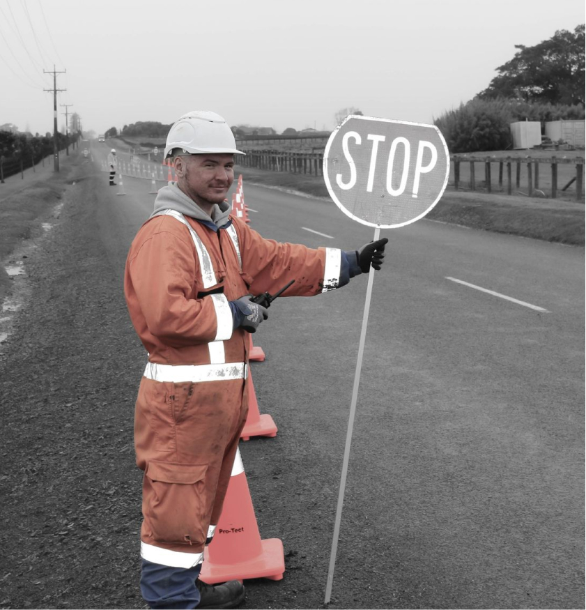Pro-Tect staff member in high-vis overalls holding a stop sign on the side of the road